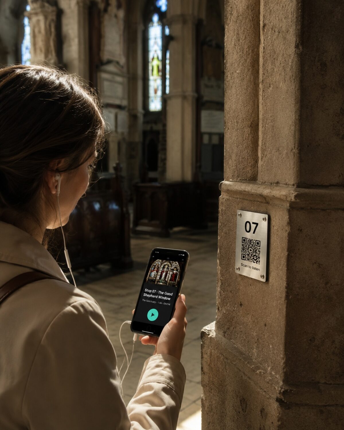 A visitor with wired earbuds stands in a church bathed in stained-glass light, holding a phone showing the Wexplo audio guide for "Stop 07 · The Good Shepherd Window, The Sanctuary." A brushed brass plate numbered 07 with a QR code labeled "Scan to listen" is mounted on the stone column beside her.